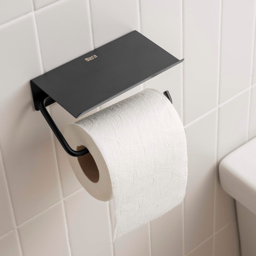 Lifestyle image of the Roca Sonata Matt Black Toilet Roll Holder with Cover mounted on a bathroom wall with toilet paper in holder